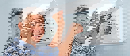 A technician in a blue shirt is shown servicing an air conditioner